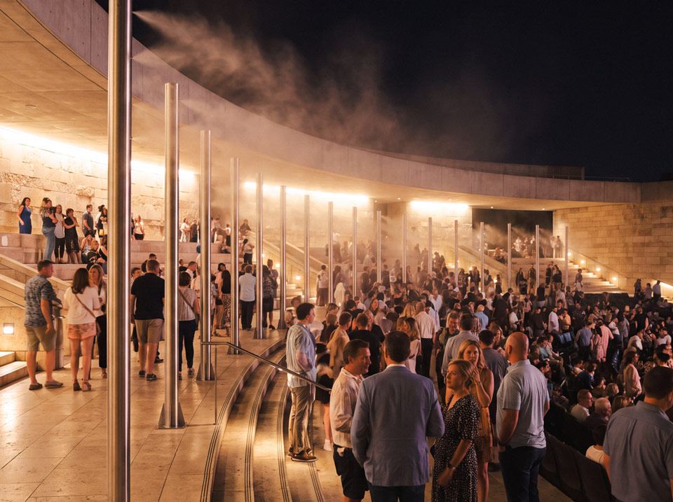 Evening outdoor event with tall misting poles creating fog cooling above the crowd
